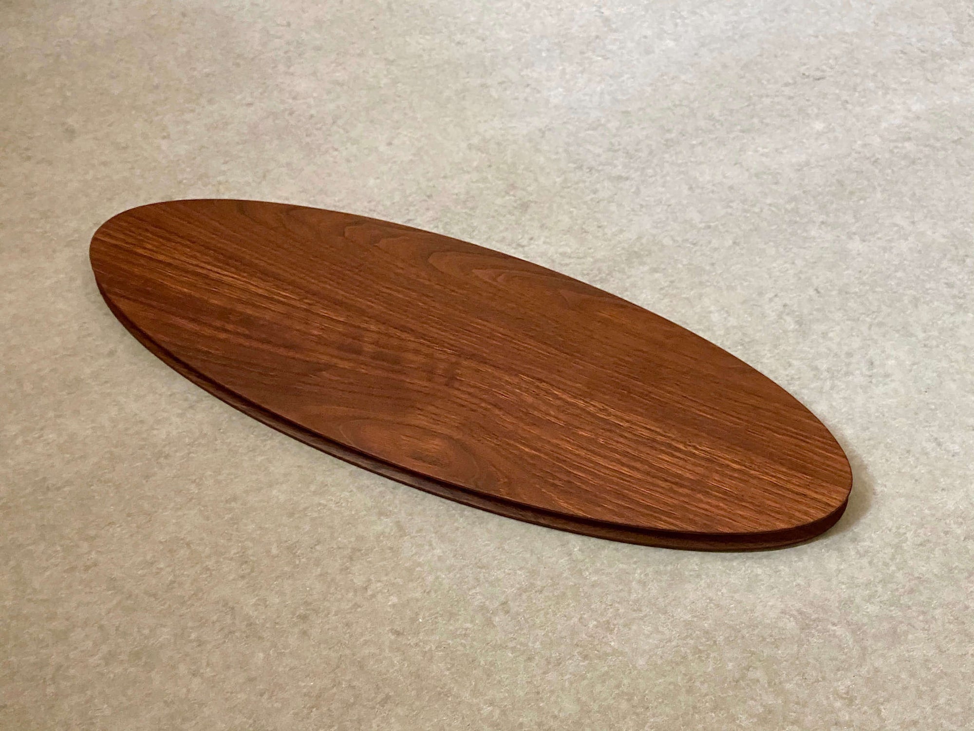 A large ellipse shaped cutting and serving board made of mahogany. Sculpted edges provide a nice detail.