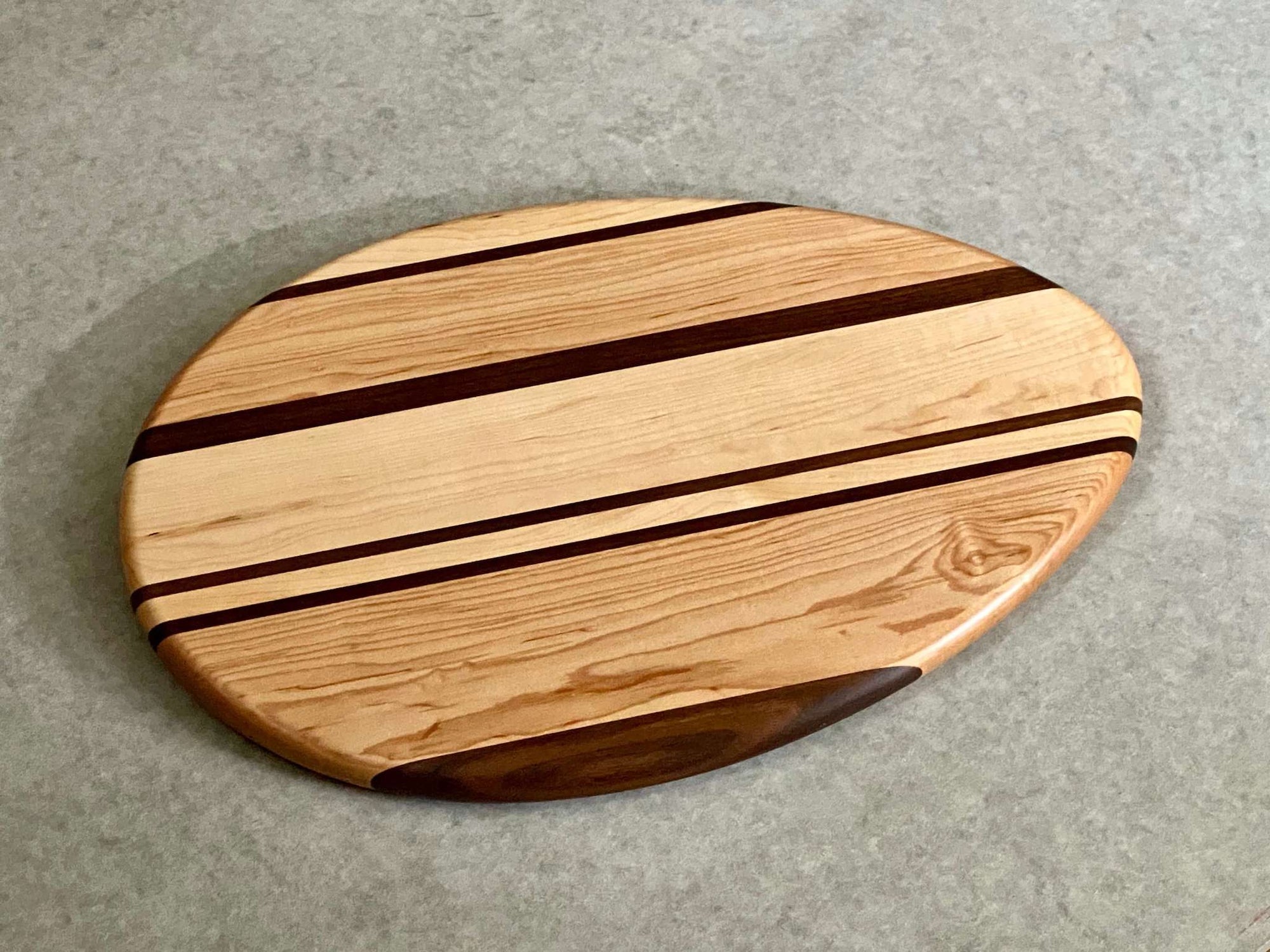 An egg shaped cutting and serving board with bold stripes of mahogany and walnut.