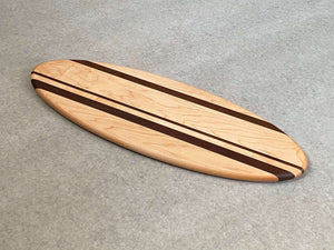A large ellipse shaped cutting and serving board made of maple with thin stripes of walnut. 