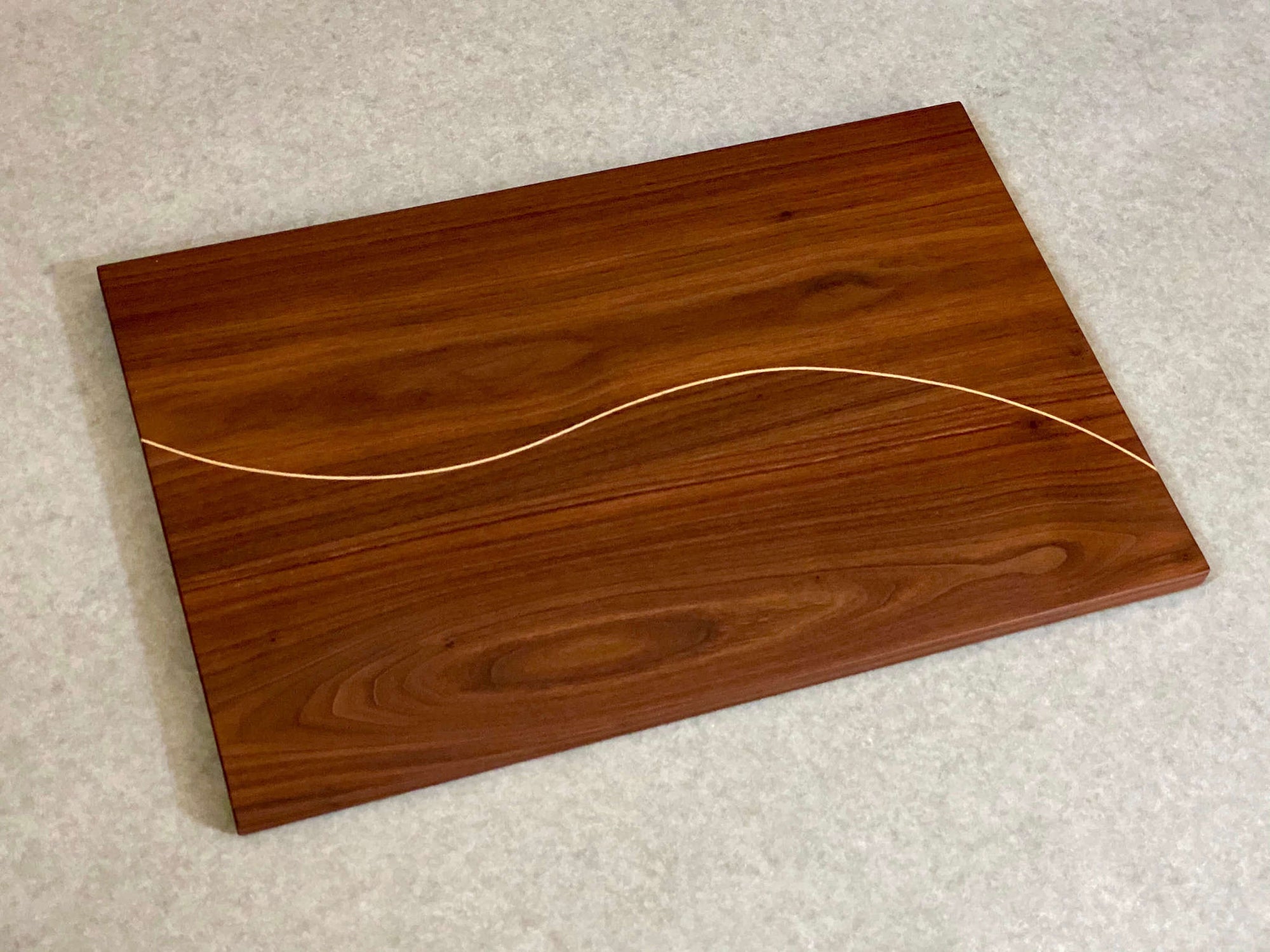 A rectangular cutting and serving board made of walnut with a thin line of maple curving down the center.
