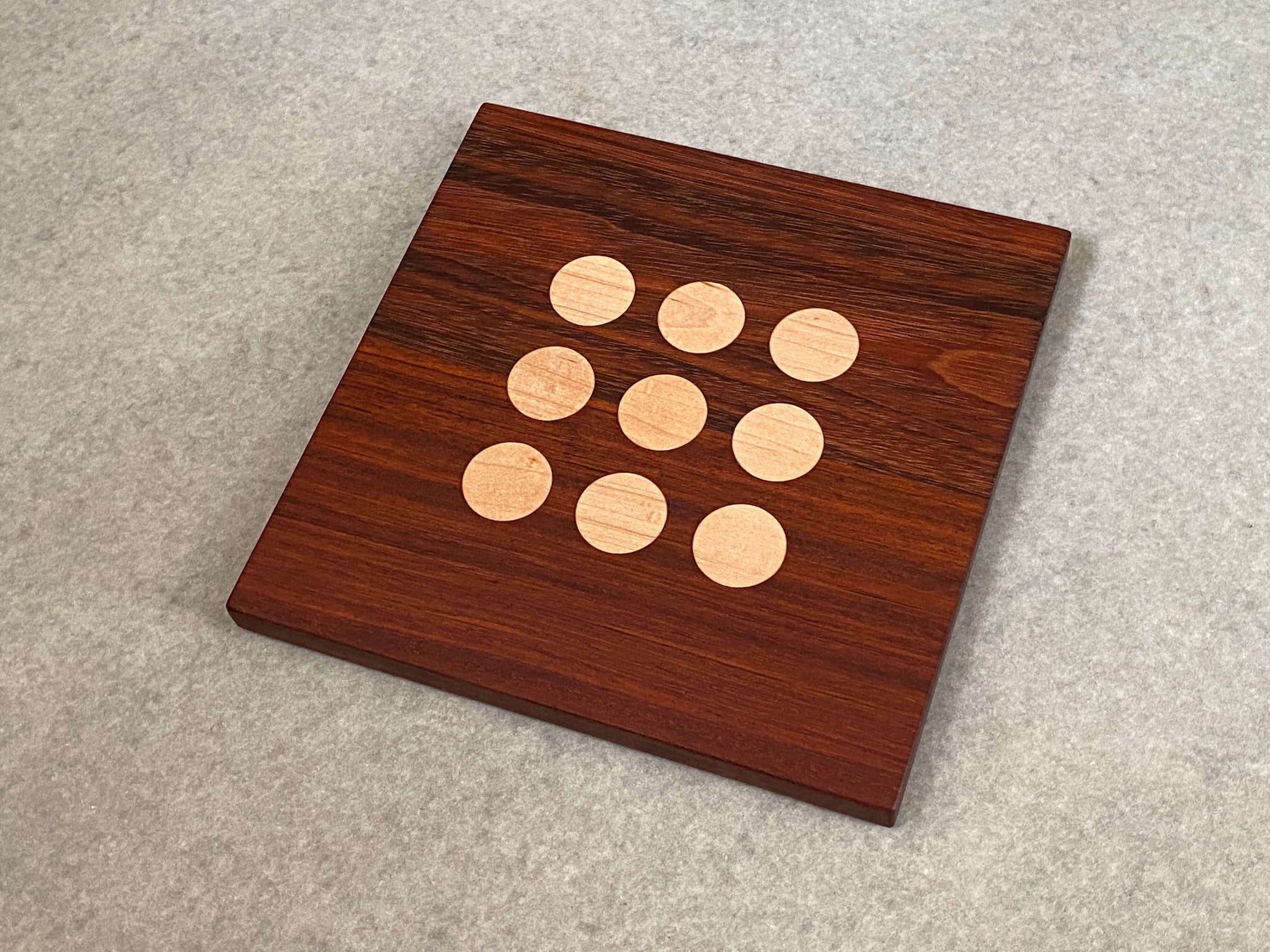 Square cutting and serving board in white oak with 9 inlaid maple dots like tic tac toe.