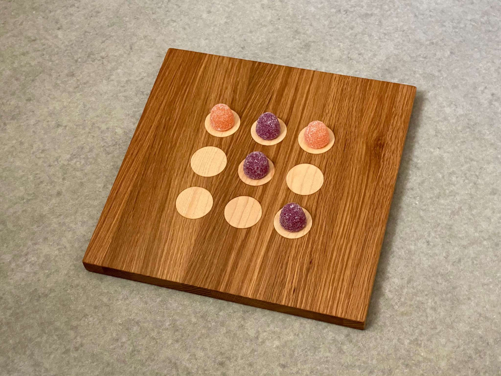 Square cutting and serving board in white oak with 9 inlaid maple dots like tic tac toe.