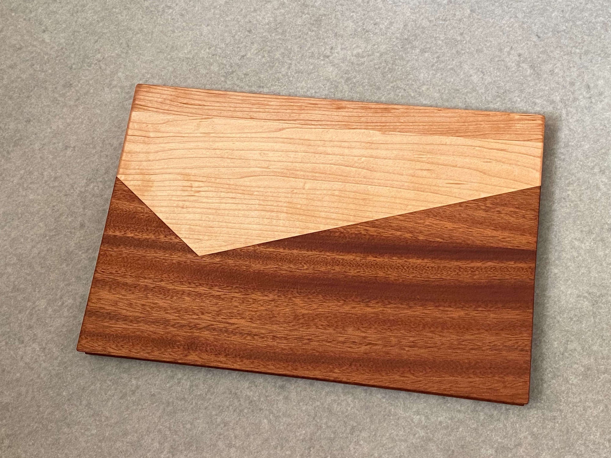A rectangular board made of two shapes pieced together that resemble a maple mountain against a mahogany background. Sculpted edges provide natural fingerholds.