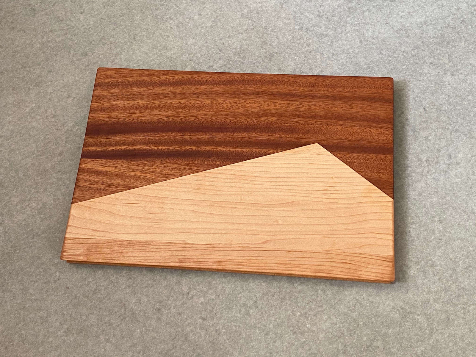 A rectangular board made of two shapes pieced together that resemble a maple mountain against a mahogany background. Sculpted edges provide natural fingerholds.