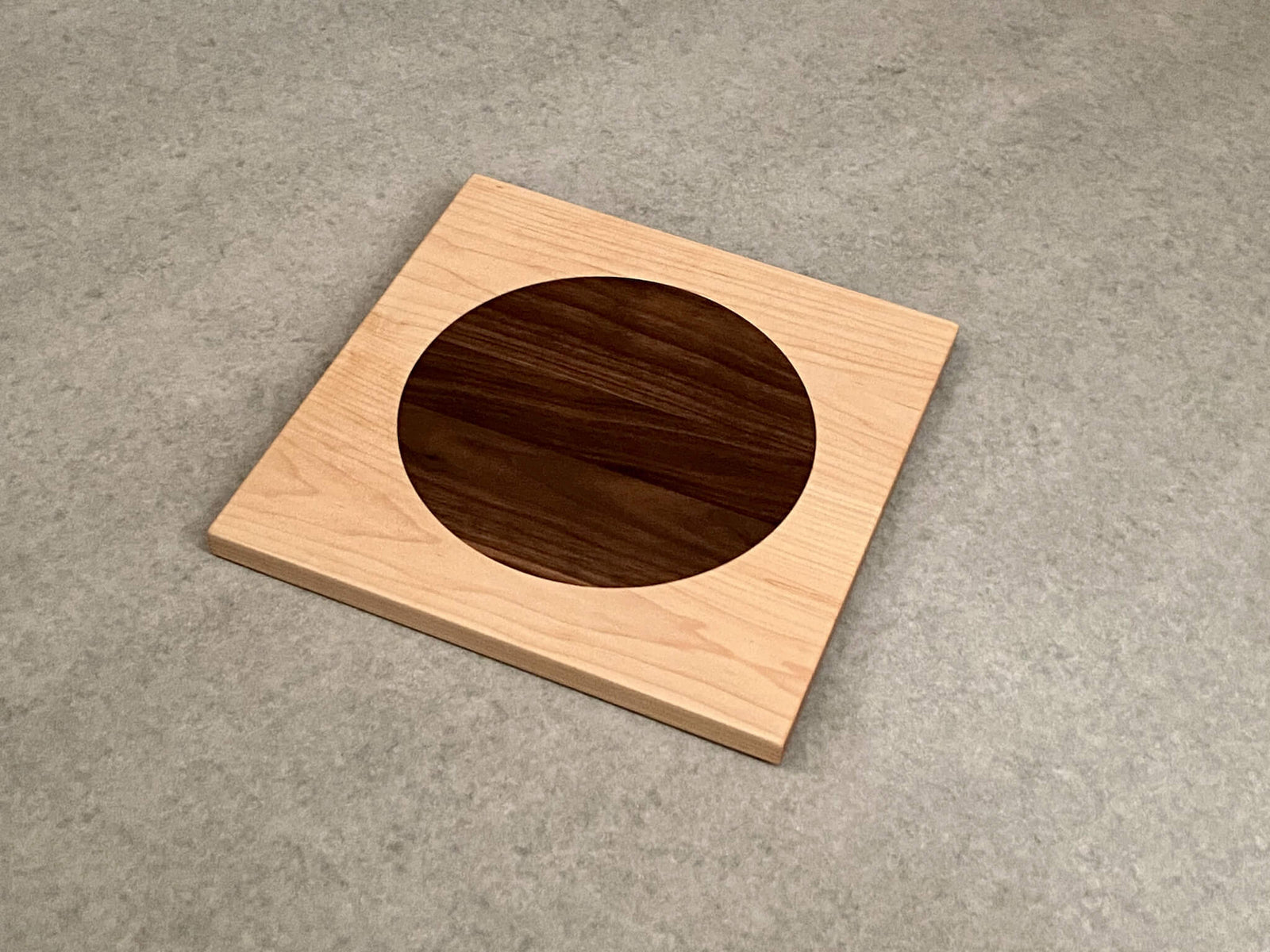 Square cutting board in walnut with large inlaid disc of white oak.