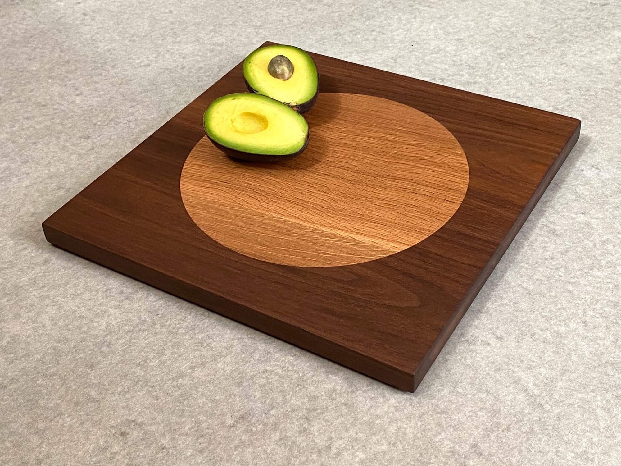 Square cutting board in walnut with large inlaid disc of white oak.