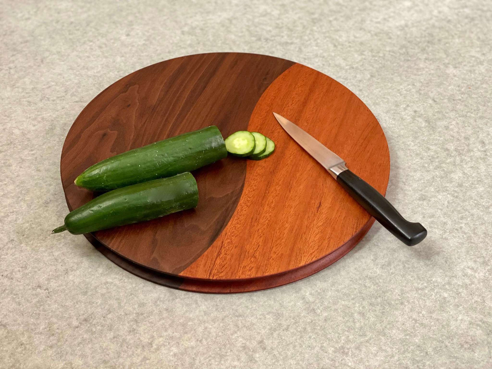 A round cutting and serving board made of part walnut and part mahogany with an off center curving joint. Sculpted edges provide a nice detail.