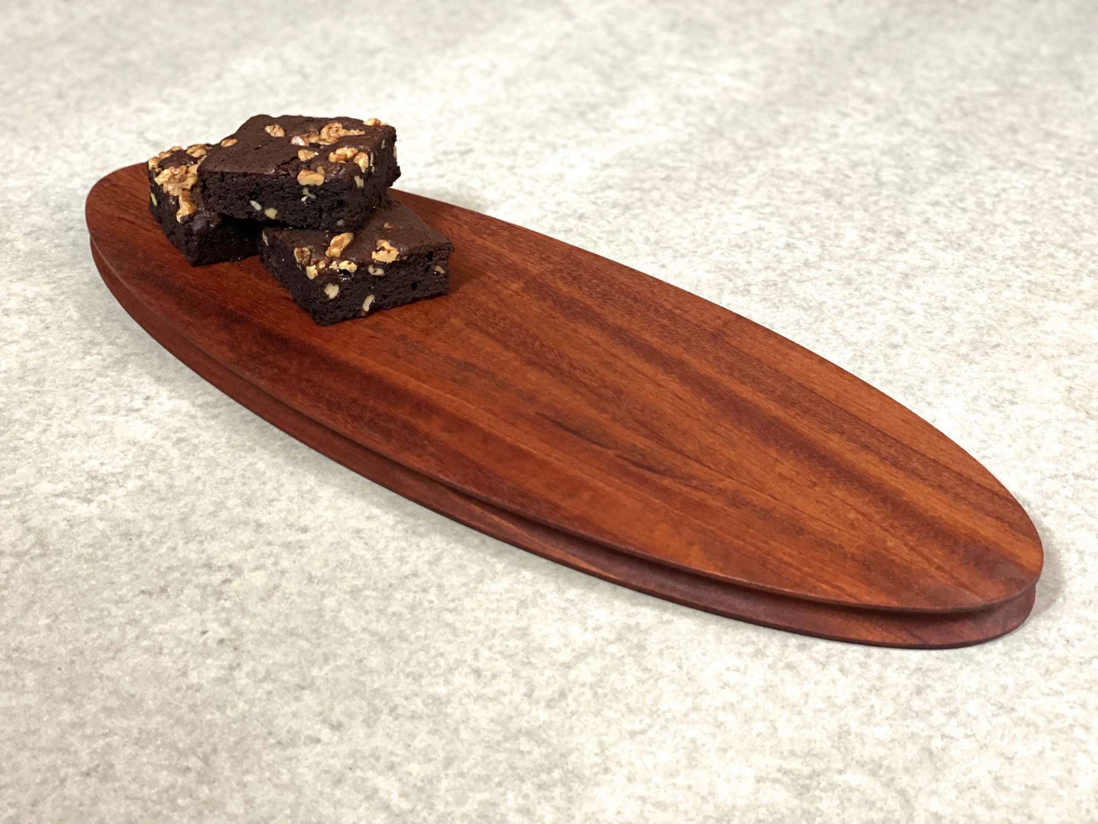 A large ellipse shaped cutting and serving board made of mahogany. Sculpted edges provide a nice detail.