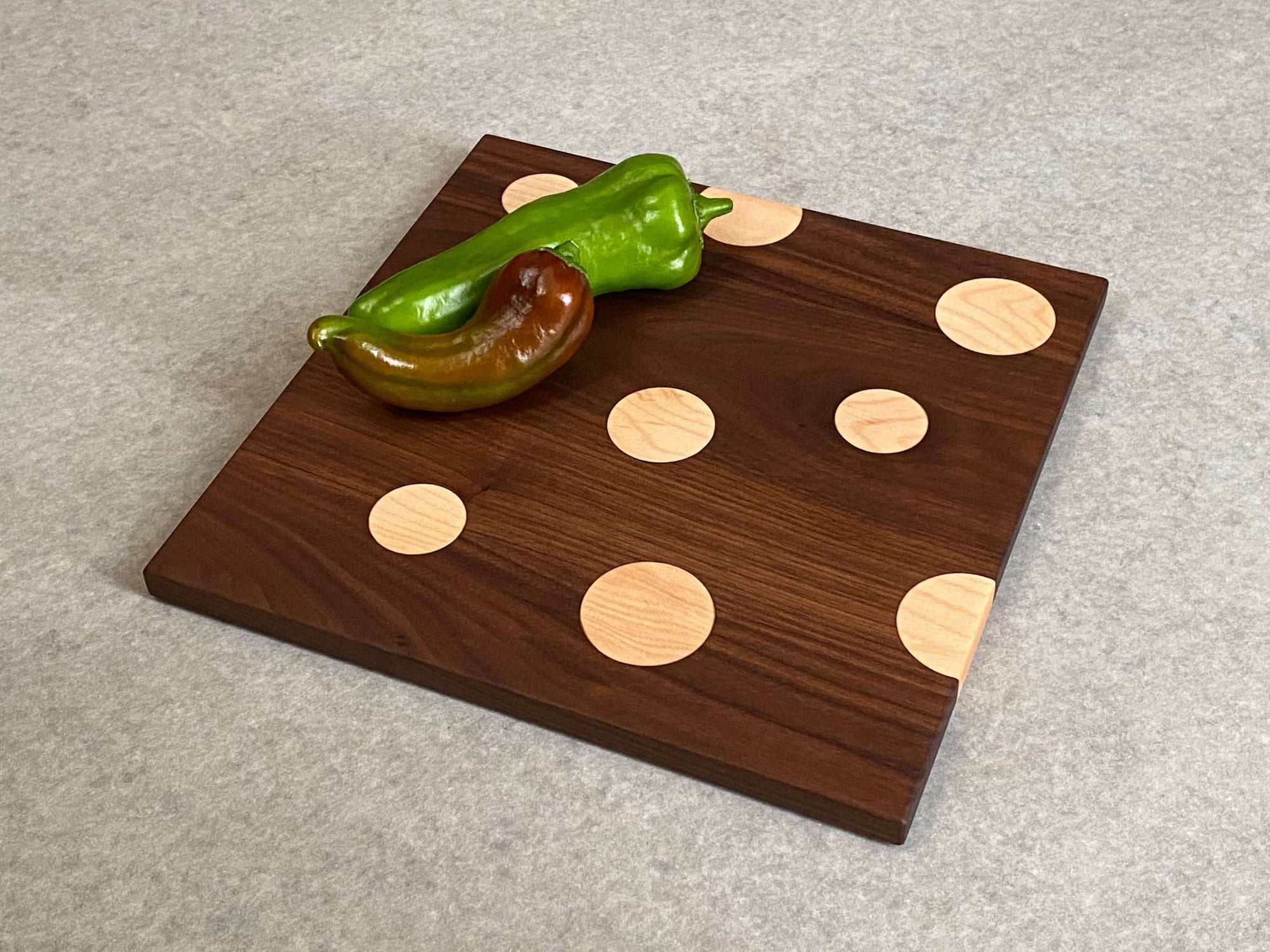 Square cutting and serving board in walnut with inlaid maple dots.
