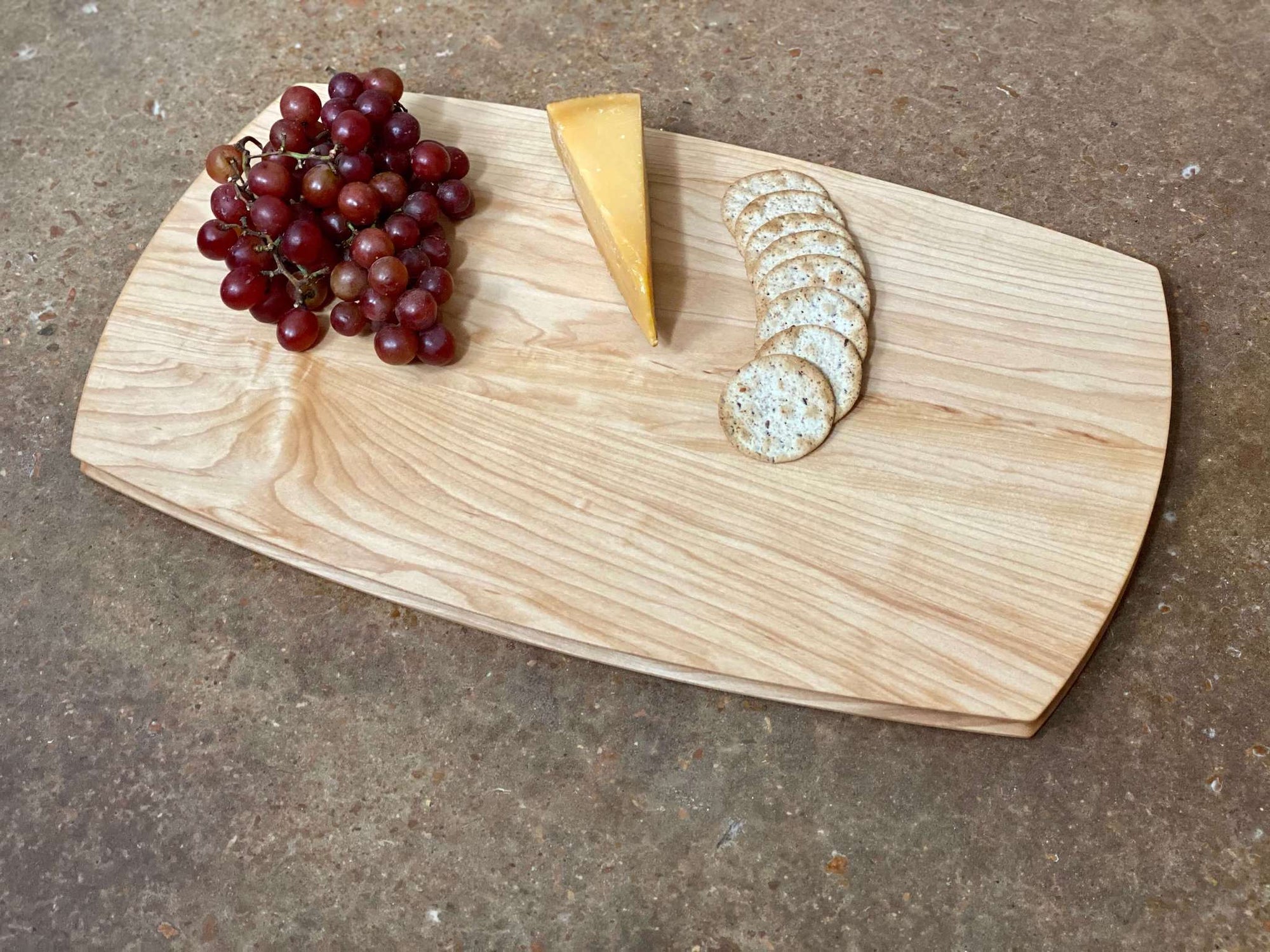 A large rounded rectangular cutting and serving board made of maple. Sculpted edges provide comfortable fingerholds.