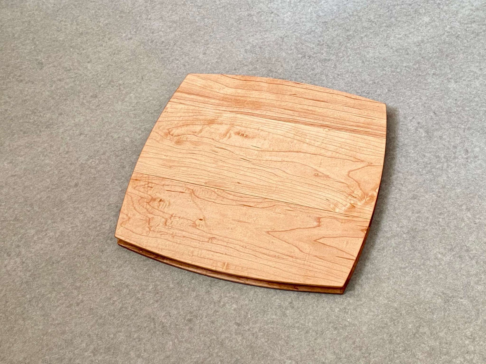 A rounded square cutting and serving board in mahogany. Sculpted edges provide a nice detail.