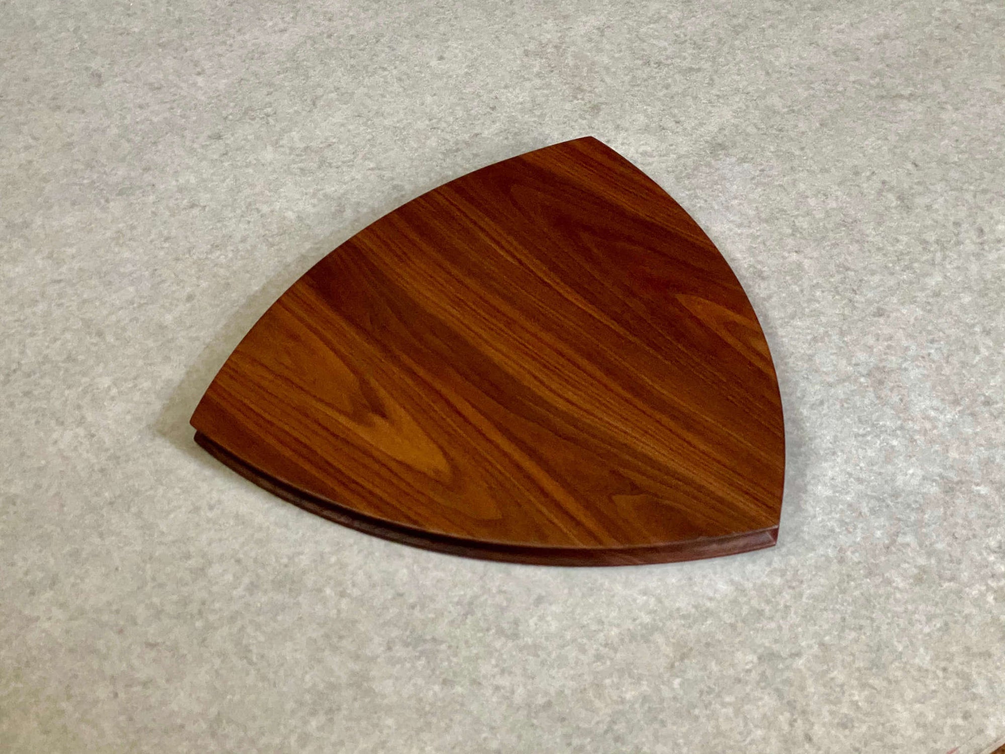 A rounded triangular shaped cutting and serving board in mahogany. Sculpted edges provide a nice detail.