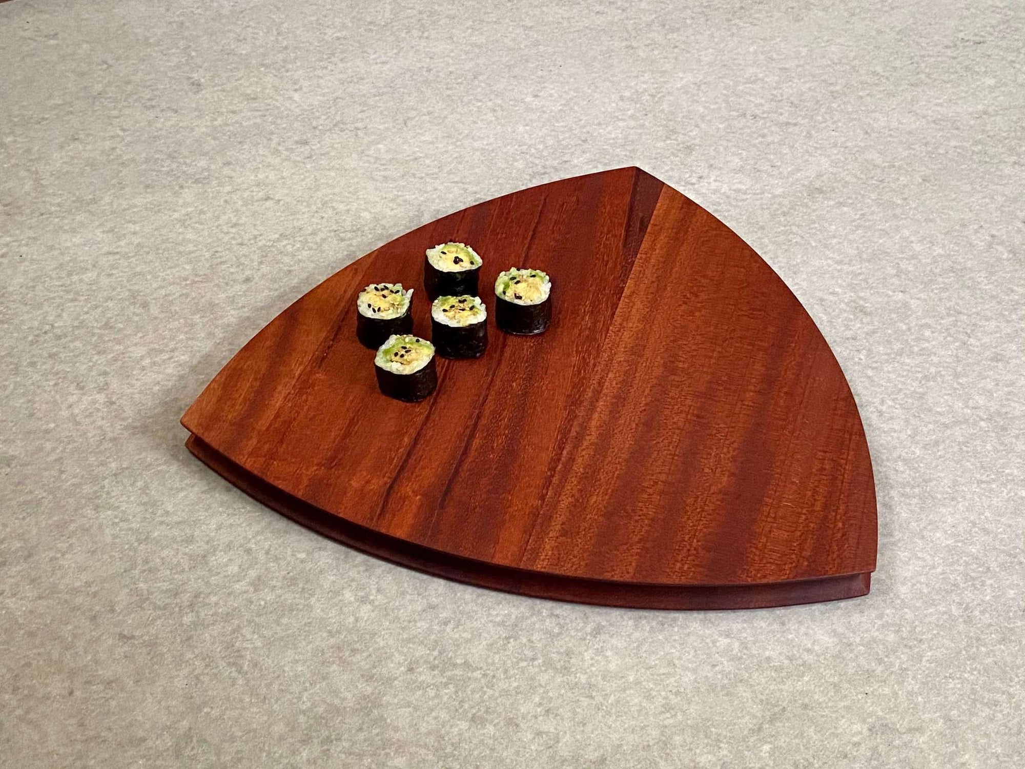 A rounded triangular shaped cutting and serving board in mahogany. Sculpted edges provide a nice detail.