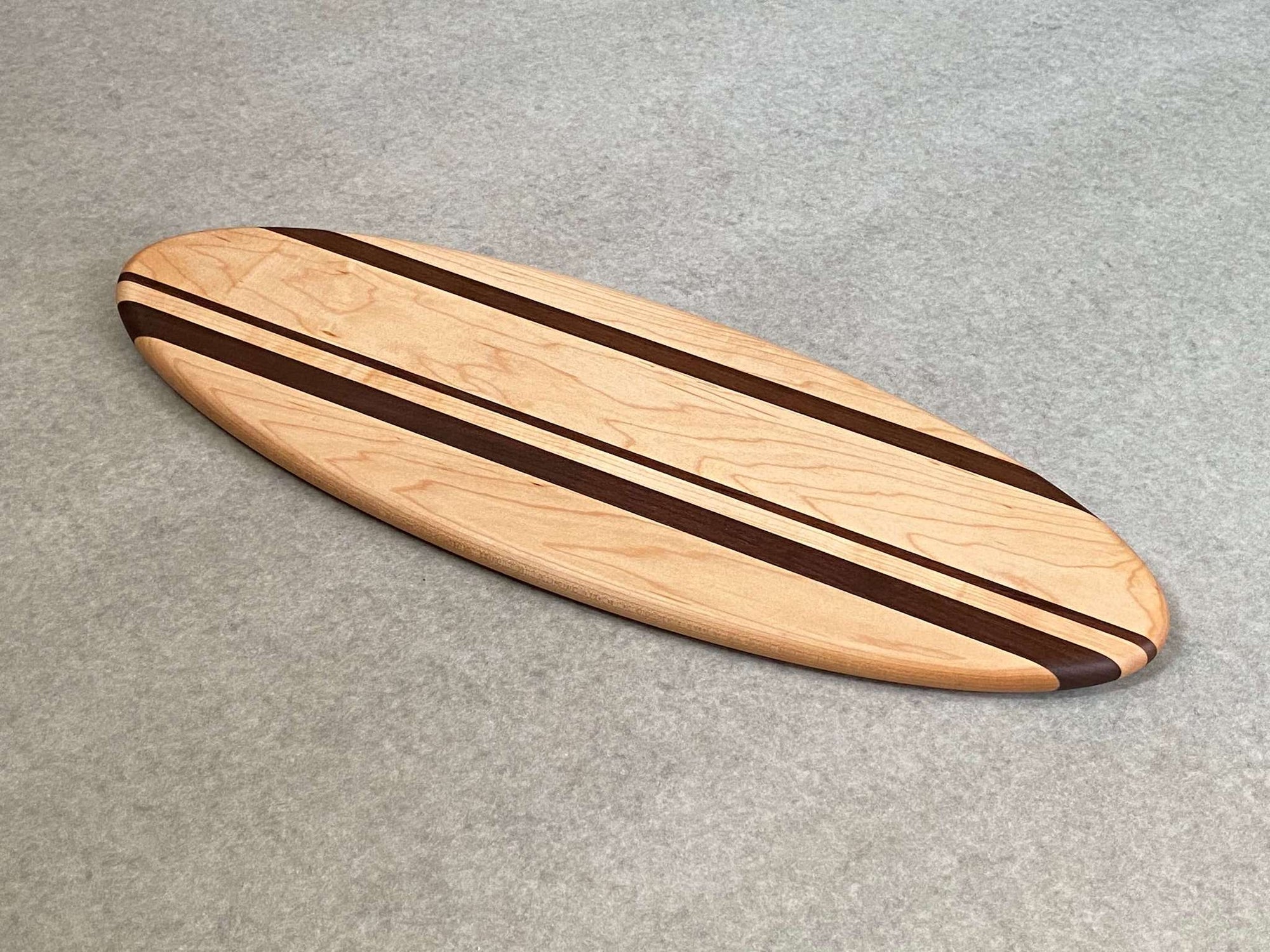 A large ellipse shaped cutting and serving board made of mahogany with thin stripes of walnut. 