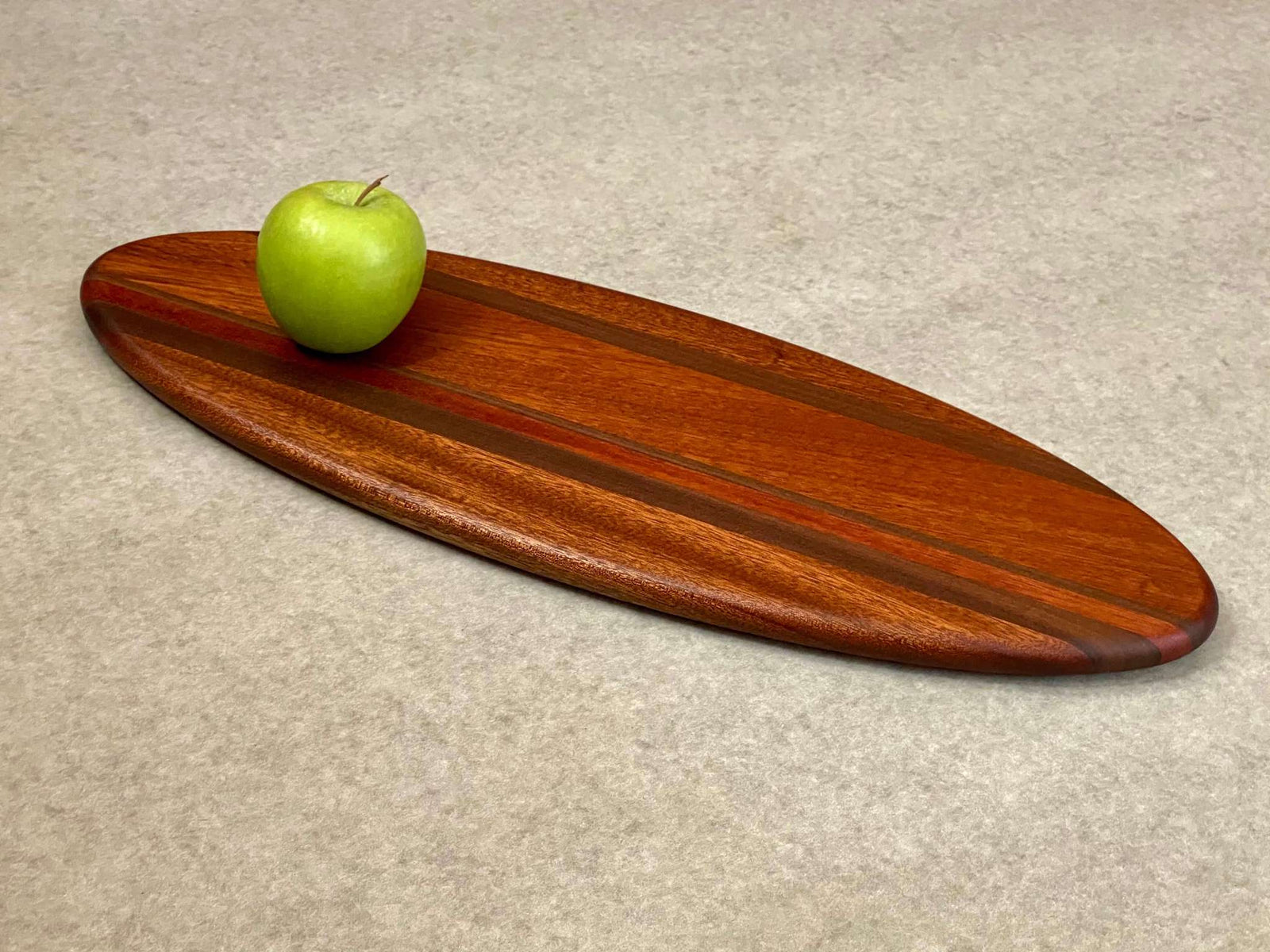 A large ellipse shaped cutting and serving board made of mahogany with thin stripes of walnut. 