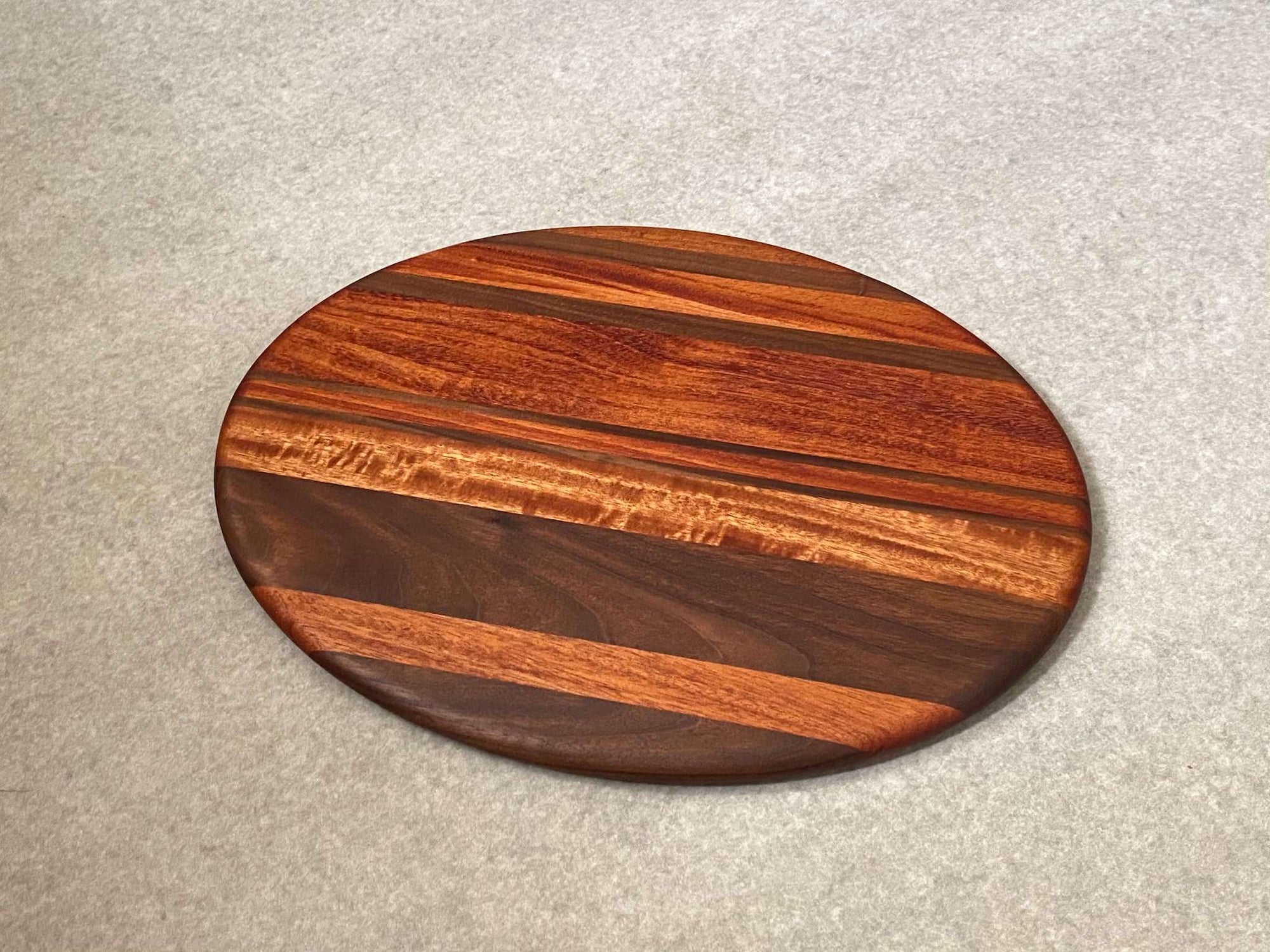 Oval shaped cutting and serving board in maple with walnut stripes.