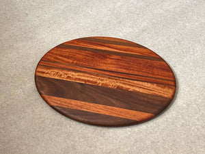 Oval shaped cutting and serving board in mahogany with walnut stripes.