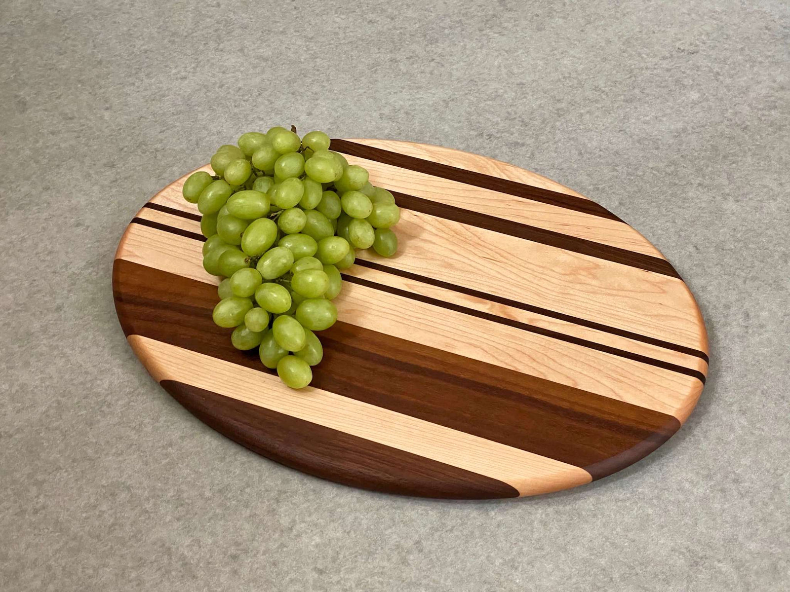 Oval shaped cutting and serving board in maple with walnut stripes.