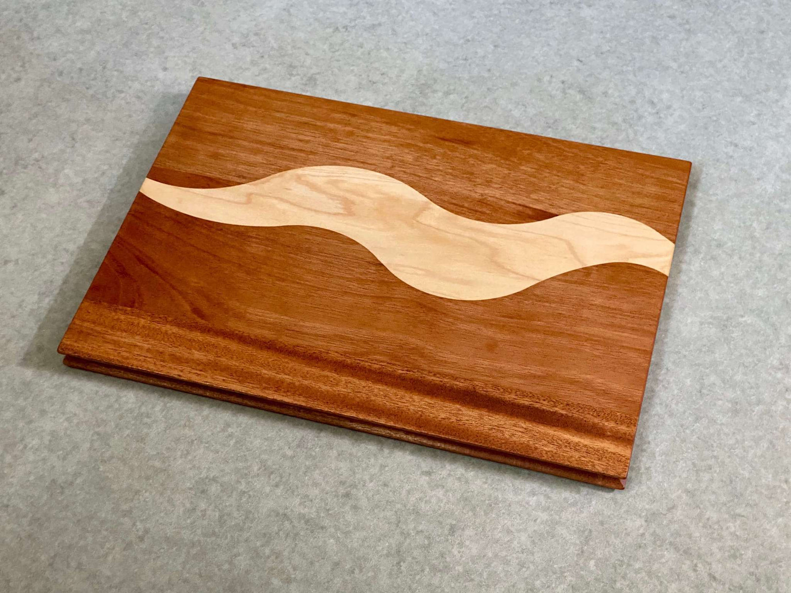 A rectangular cutting and serving board of mahogany with a bold squiggly stripe of maple. Sculpted edges provide comfortable fingerholds.