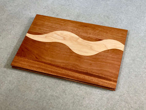 A rectangular cutting and serving board of mahogany with a bold squiggly stripe of maple. Sculpted edges provide comfortable fingerholds.