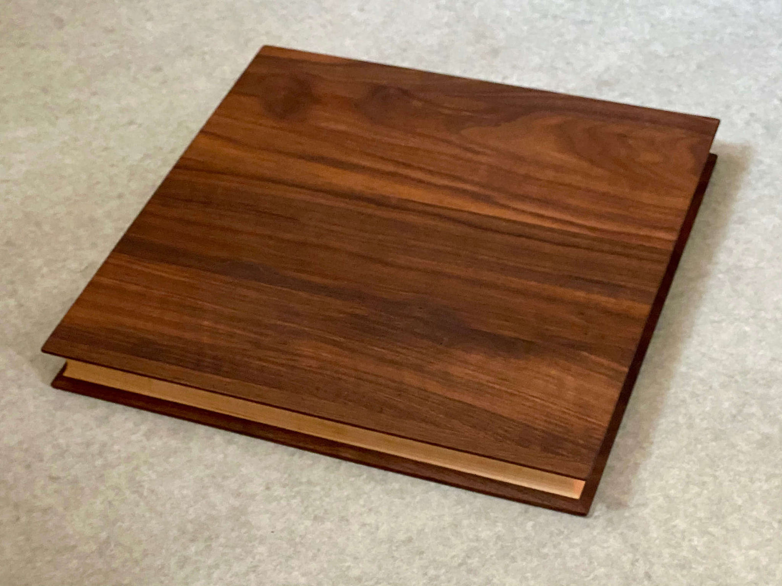 A square cutting and serving board of maple sandwiched between two thin layers of walnut. Sculpted edges provide comfortable fingerholds.