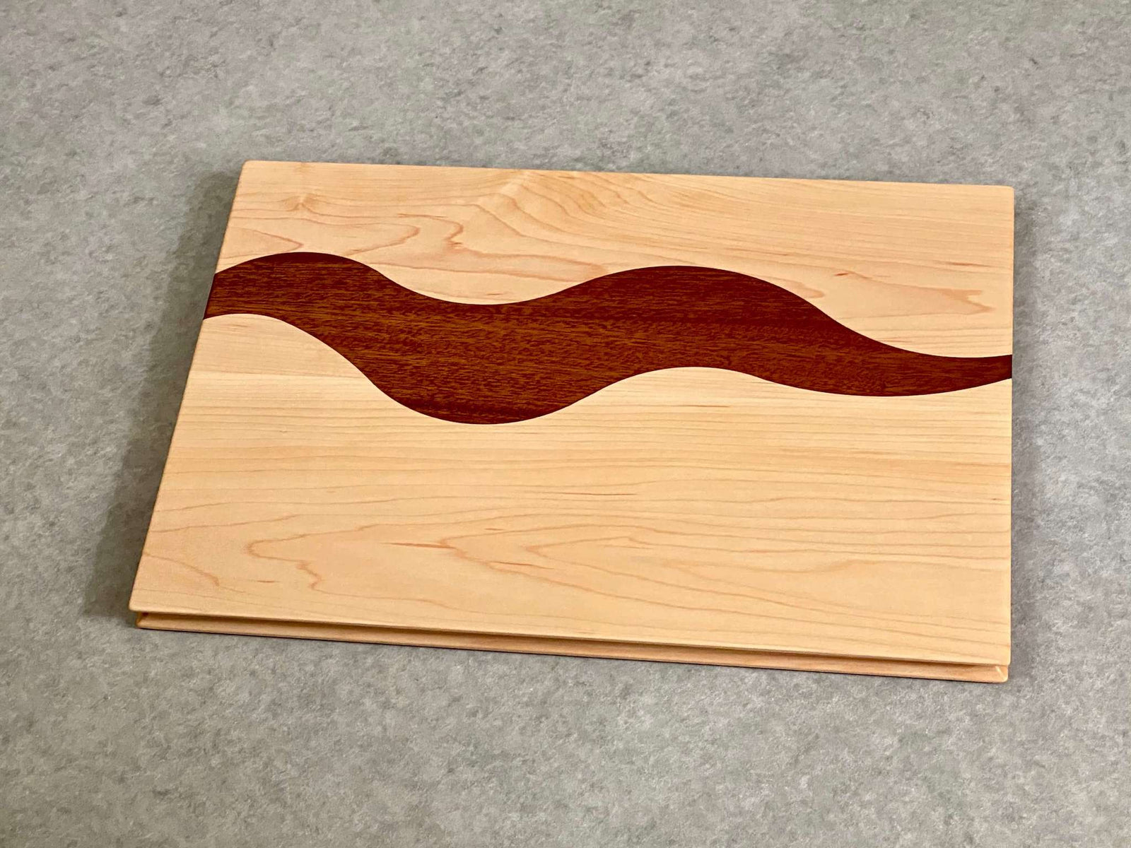 A rectangular cutting and serving board of mahogany with a bold squiggly stripe of maple. Sculpted edges provide comfortable fingerholds.