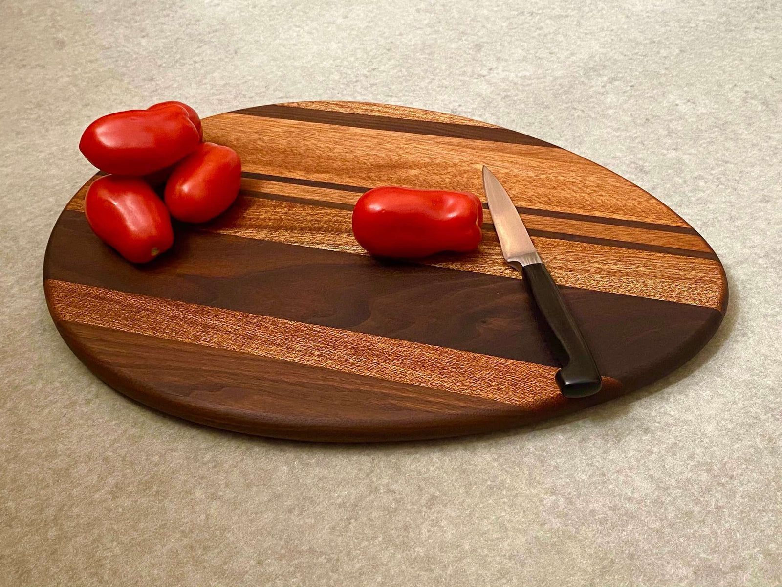 An egg shaped cutting and serving board with bold stripes of mahogany and walnut.